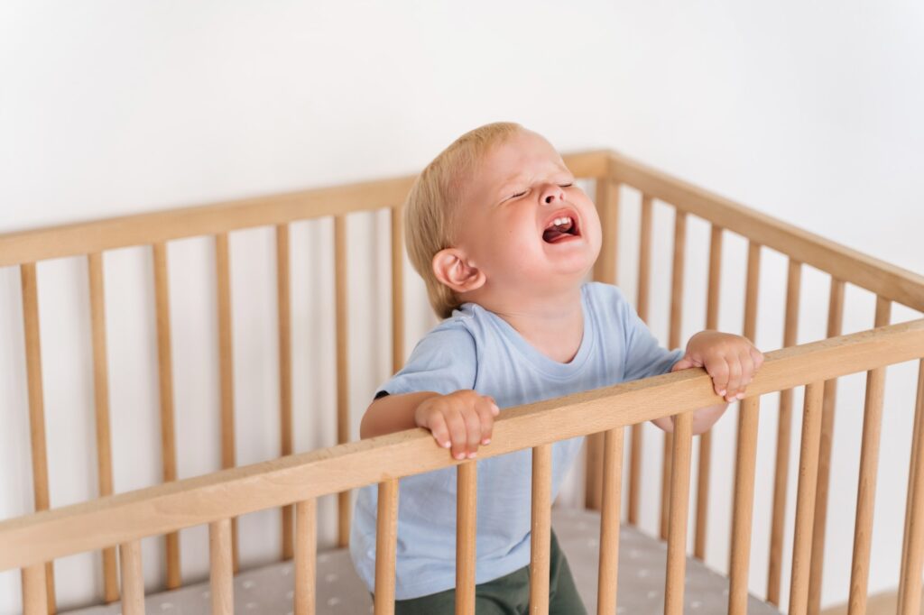 Portrait of upset crying baby standing in crib getting hysterical seeking attention of parents