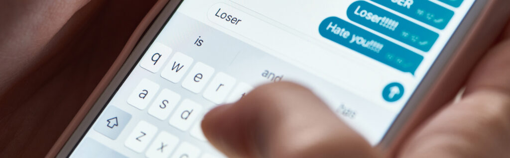 panoramic shot of abuser typing offensive messages while using smartphone, illustrative editorial
