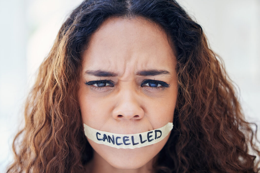 Portrait of a young woman with tape on her mouth that has the word cancelled written on it